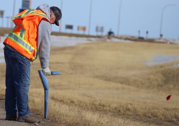 A utility locator marking lines on the side of a highway.