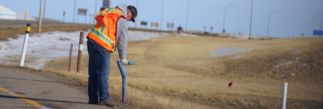 A utility locator marking lines on the side of a highway.